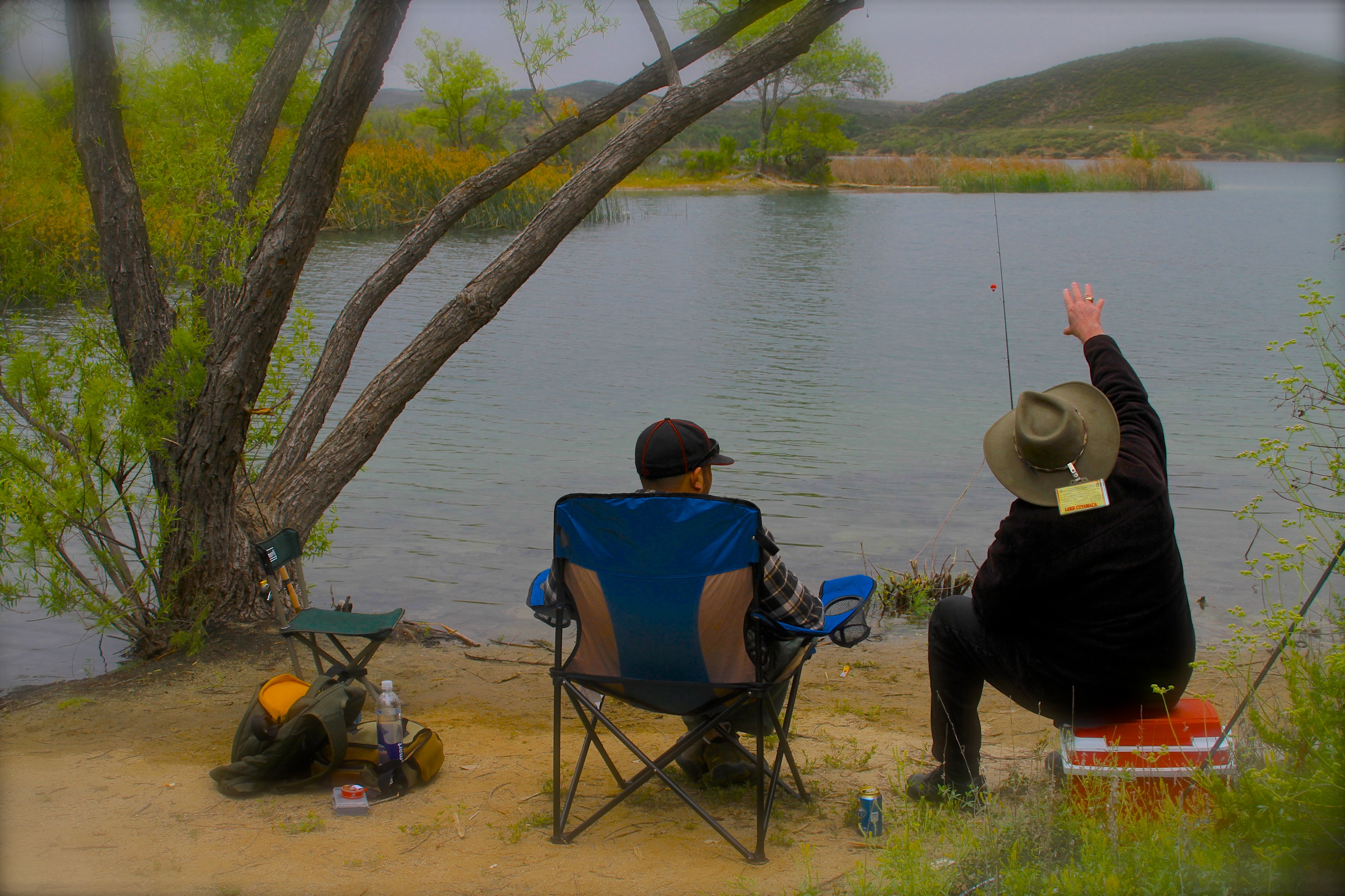 Two people fishing by a lake with chairs and equipment.